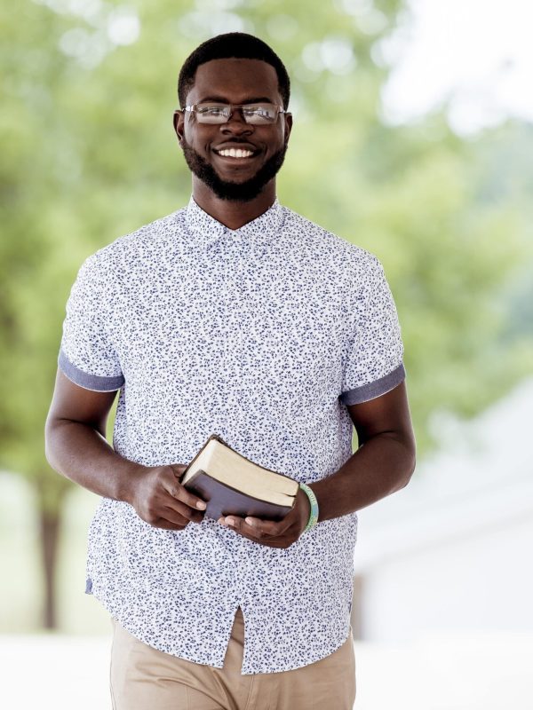 shallow-focus-shot-male-standing-while-holding-bible-looking-camera-min