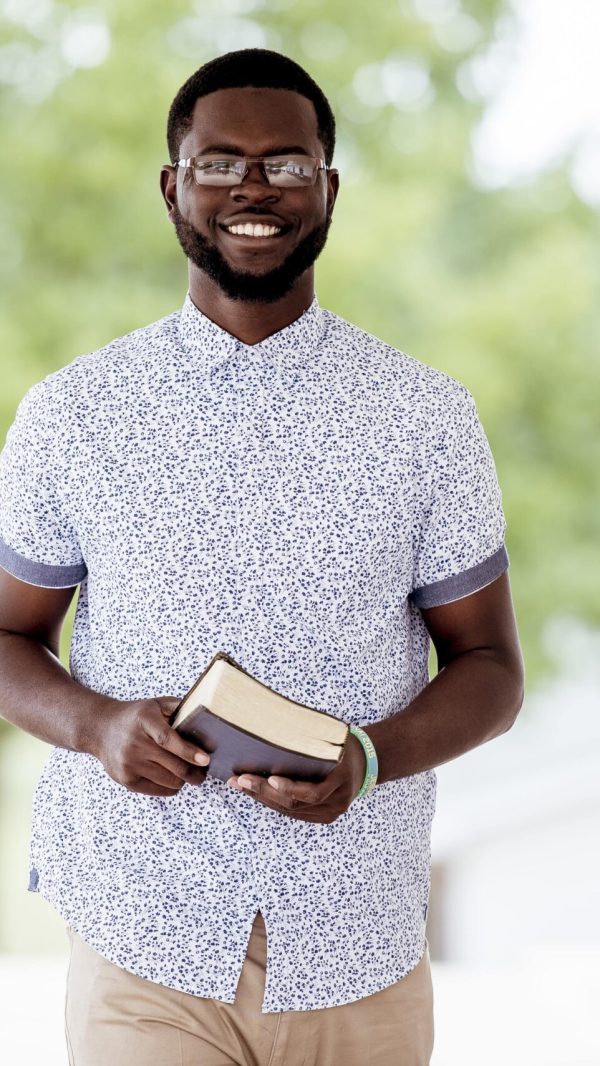 shallow-focus-shot-male-standing-while-holding-bible-looking-camera-min